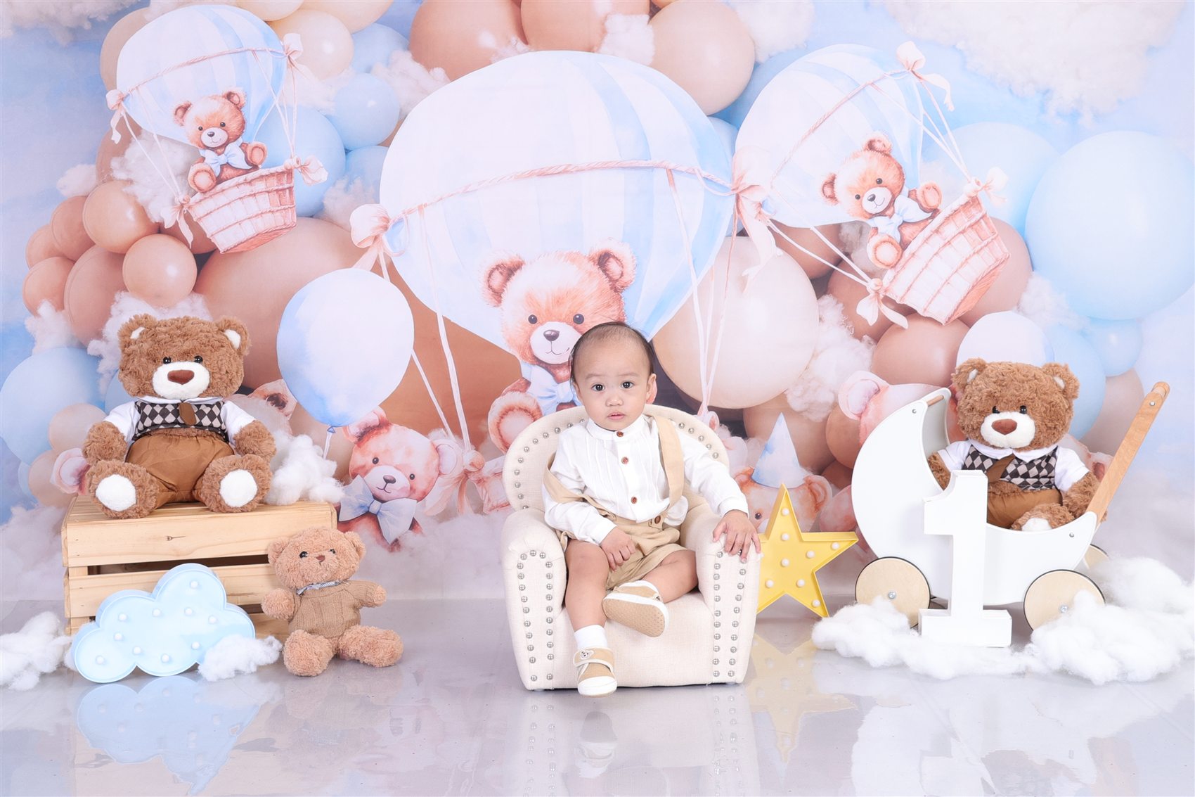 Jaden Matthew seated in his first birthday backdrop with teddy bears, balloons, and clouds